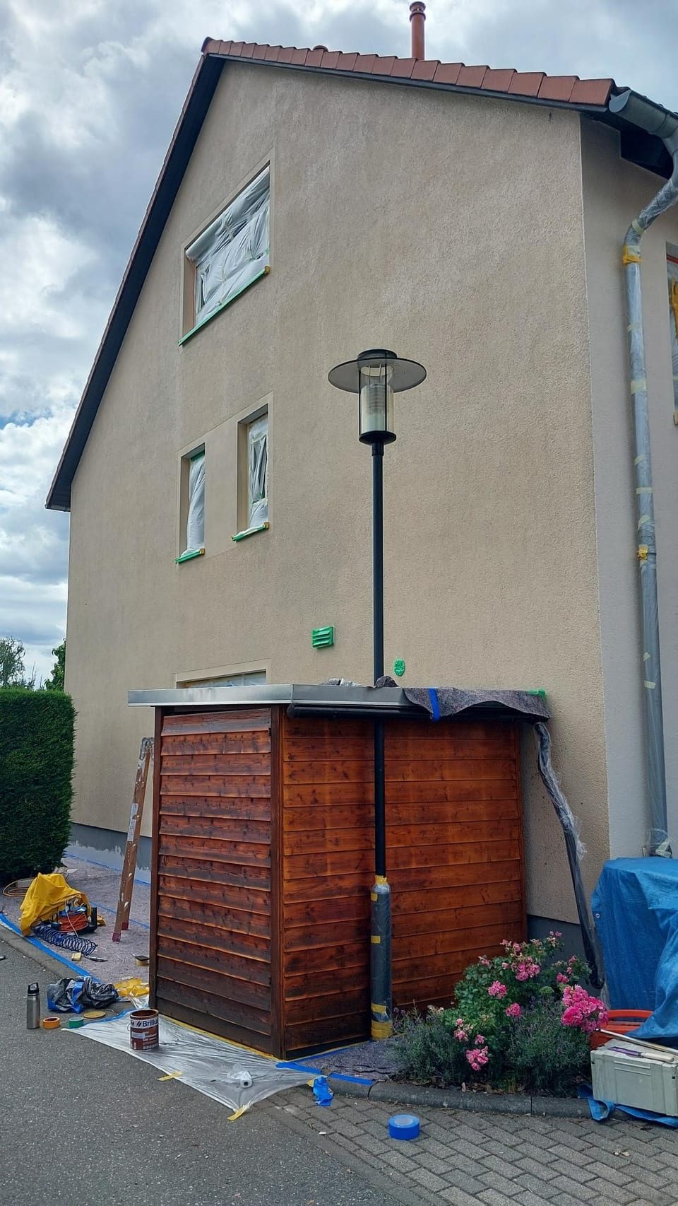 Giebelseite eines Wohnhauses vor dem Anstrich: verwitterter beiger Putz, abgeklebte Fenster, Abdeckplanen und Leiter davor